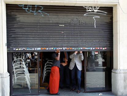 Unos trabajadores bajan la persiana de un bar en Barcelona.