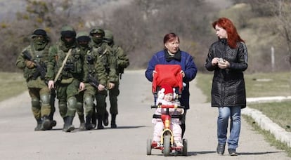 Dos mujeres caminan con un beb&eacute; junto a hombres armados en los alrededores de Simfer&oacute;pol, Crimea. 