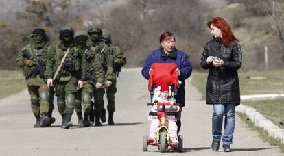 Dos mujeres caminan con un bebé junto a hombres armados en los alrededores de Simferópol, Crimea.