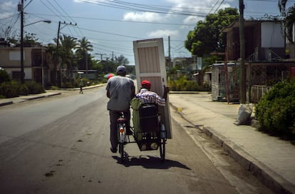 Un hombre transporta la puerta de una vivienda en el lado del pasajero de un taxi bicicleta en Holguin (Cuba).