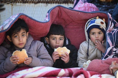 Tres niños comían pan sentados bajo una manta en la ciudad turca de Kahramanmaras, dos días después de que temblara la tierra en la región.