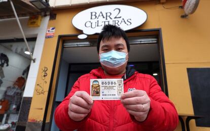 Juan, propietario del bar Dos Culturas de Zaragoza, muestra uno de los décimos agraciados con el quinto premio 86986.