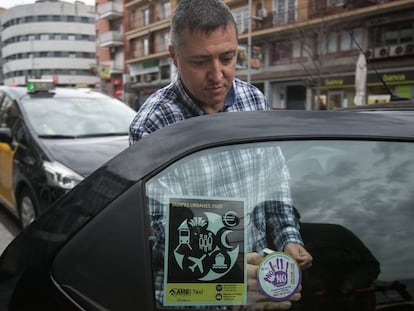 Un taxista coloca en su automóvil una pegatina de la campaña violeta.