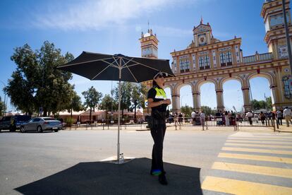 Una policía local de Sevilla se protege del sol bajo una sombrilla ubicada frente a la portada de la Feria, cuyo diseño está inspirado en dos edificios regionalistas, la plaza de España, y el Teatro Coliseo España.
