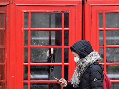 Una mujer con mascarilla protectora revisa su teléfono móvil mientras camina por Londres.