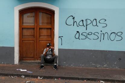 Un hombre descansa y come junto a un graffiti que dice "Chapas asesinos" durante una protesta contra las medidas de austeridad del presidente de Ecuador, Lenin Moreno, en Quito. 