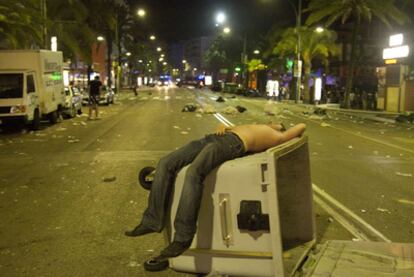 Un joven duerme sobre un contenedor de basura volcado en la calle principal de Lloret de Mar.