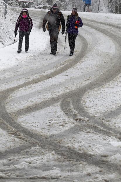 Unas personas caminan por una carretera nevada en la Sierra de Madrid.