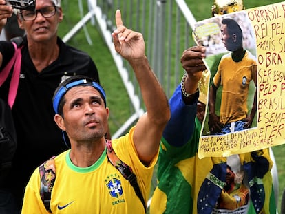 Un aficionado  brasileño señala al cielo mientras espera la cola para dar el último adiós a la leyenda del fútbol, Pelé, en el interior del estadio Urbano Caldeira, donde juega el Santos.