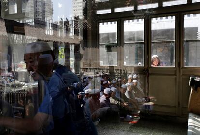 Personas reflejadas en una ventana esperando entrar en la mezquita Niujie para la oración de la mañana el día de la fiesta del sacrificio, en Pekín (China).