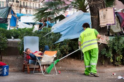 Un joven descansa en la plaza de Catalunya, mientras los servicios de limpieza trabajan a su lado, después de que los indignados hayan decidido levantar la acampada.