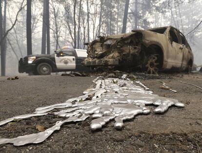 Un coche de policía pasa el viernes pasado junto a un vehículo chamuscado por el incendio que desde hace varios días asola Paradise, en California (EE UU).