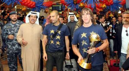 Pep Guardiola, agarrado del brazo por el presidente del club Kazma Sporting, y Puyol, con el trofeo del Mundial de Clubes, ayer a la llegada del Barcelona a Kuwait.