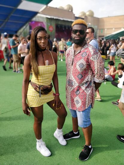 Las zapas no fallan en cualquier festival. De hecho, el look suele empezar por los pies. Ella ha elegido unas blancas abotinadas que encajan sin fisuras con el vetsido amarillo y la riñonera (que lleva años volviendo y ya está aquí). Las uñas amarillas, fantasía. Él, a la altura de su colega: camisa estampada con guiños 'oversized', pantalón corto (por debajo de la rodilla, así muy hetero) y zapatillas negras.