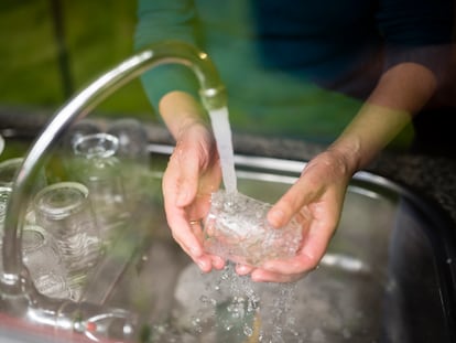 Detalle de unas manos enjuagando vasos en un fregadero.