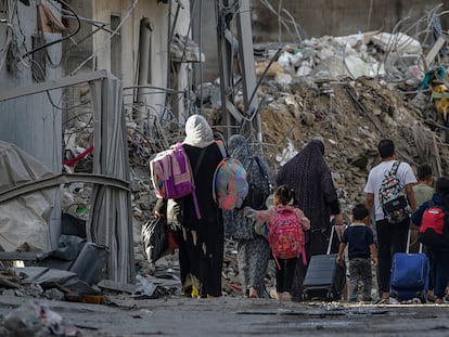 Refugiados palestinos pasan junto a varios edificios destruidos tras los ataques aéreos israelíes, este martes.