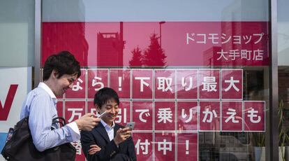 Dos hombres miran sus teléfonos delante del escaparate de una tienda de NTT DOCOMO en Tokio, Japón.