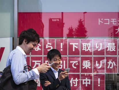 Dos hombres miran sus tel&eacute;fonos delante del escaparate de una tienda de NTT DOCOMO en Tokio, Jap&oacute;n.