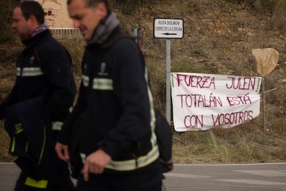 Dos bomberos pasan junto a un cartel en apoyo a Julen, el 22 de enero de 2019.