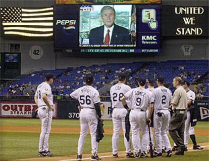 Los jugadores del equipo de béisbol de Tampa siguen la intervención de George W. Bush antes del inicio del partido.