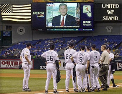 Los jugadores del equipo de béisbol de Tampa siguen la intervención de George W. Bush antes del inicio del partido.