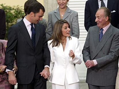 La Reina mira los gemelos de zafiros y oro blanco regalo de Letizia Ortiz al Príncipe en la petición de mano, mientras el Rey habla con la pareja.