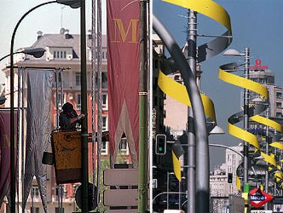 Un operario coloca banderolas en las farolas del centro de Madrid. A la derecha, adornos desplegados en la Gran Vía, por donde pasarán los novios.