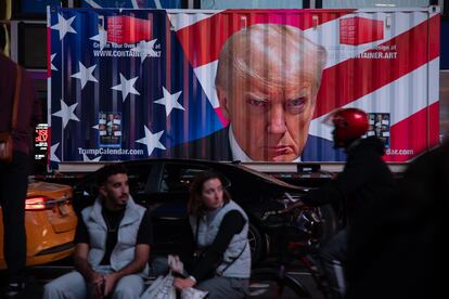 Una pareja sentada en Times Square frente a un contenedor con un retrato de Trump, la noche de las elecciones presidenciales.
