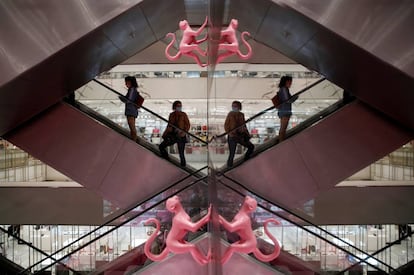 Los clientes, con mascarilla, se reflejan en un espejo mientras suben por una escalera mecánica de los grandes almacenes Le Printemps Haussmann en París.