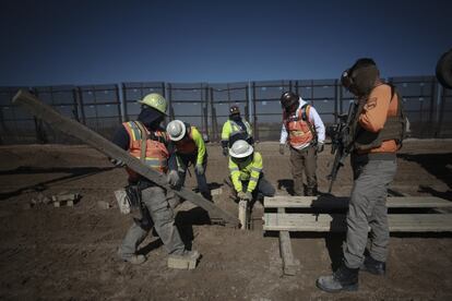 Guardas de seguridad privada vigilan mientras los trabajadores preparan los cimientos de una nueva sección del muro fronterizo.