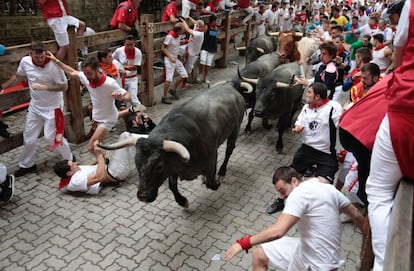 Runners scatter and fall as fighting bulls stampede through the streets of Pamplona on Saturday morning.