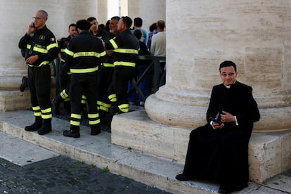 Un cura, junto a un grupo de bomberos, en un lateral de la plaza de San Pedro en el Vaticano.