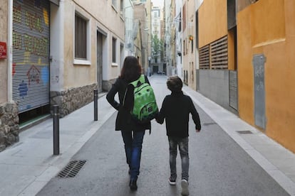 Una madre carga con la mochila de su hijo camino de la escuela.