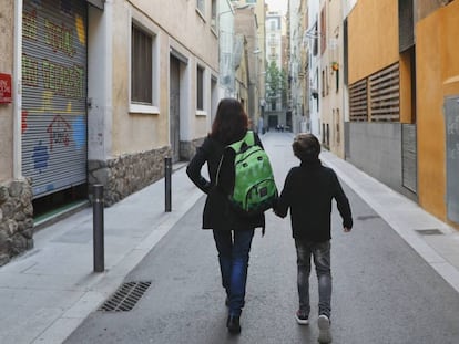 Una madre carga con la mochila de su hijo camino de la escuela.