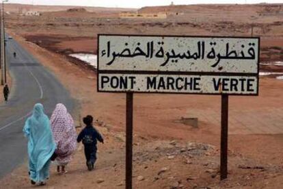 Dos mujeres y un niño pasan junto a un cartel donde se lee "Puente de la Marcha Verde".