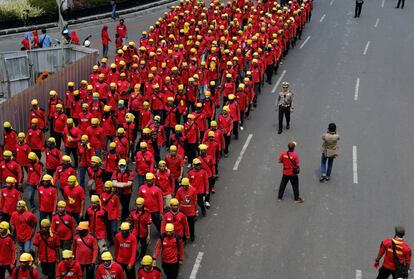 Un oficial de policía camina junto a un grupo de trabajadores indonesios que marchan para conmemorar el Día del Trabajo.