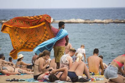 Un home ven pareos a la platja de la Barceloneta.