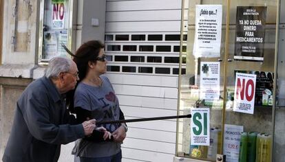 Dos usuarios contemplan los carteles que exhiben todas las farmacias de la Comunidad Valenciana.