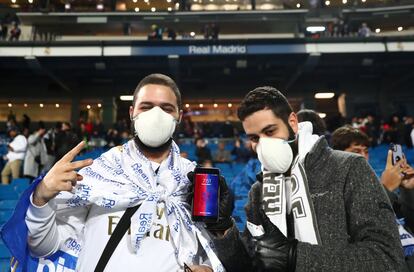 Dos aficionados con mascarillas esperan el comienzo del partido.