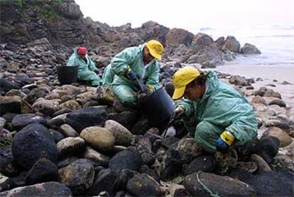 Tres personas limpian el chapapote acumulado entre las rocas en una cala de la zona de Lires (Muxía).