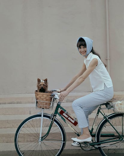 Audrey Hepburn en bicicleta, 1964. Fotografiada por el legendario Cecil Beaton, Audrey aparece montando en bicicleta. Los detalles del perrito en la cesta delantera, los cuadros vichy y el pañuelo en la cabeza aportan ese toque de dulzura inseparable de la actriz.