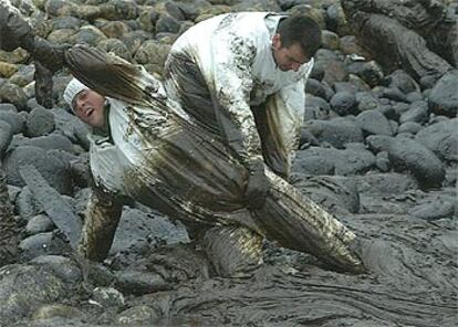 Una soldado atrapada en el chapapote es ayudada a salir por dos compañeros en una playa de Lira.