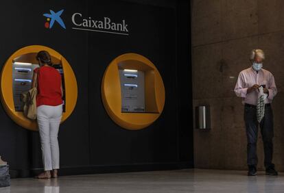 Dos personas en los cajeros dispuestos en el edificio de la sede de Caixabank, en Valencia, Comunidad Valenciana (España), a 4 de septiembre de 2020.