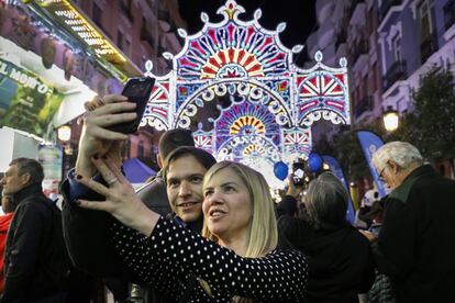 La iluminación en las calles es uno de los elementos característicos de las Fallas. En la imagen, unos turistas se hacen un fotografía junto a las luces ornamentales que estos días decoran las calles de Valencia.
