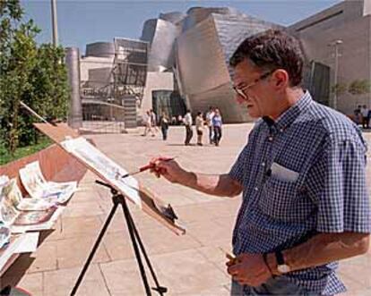 Un artista callejero pintaba ayer cuadros junto al Museo Guggenheim de Bilbao.