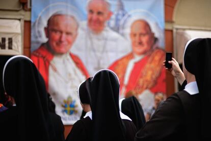 Varias monjas observan y fotografían un panel con la imagen de varios pontífices. 