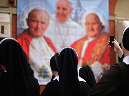 Varias monjas observan y fotografían un panel con la imagen de varios pontífices. 