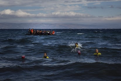 Llegada de botes atestados de refugiados a la isla de Lesbos y, en primer plano, tres socorristas para ayudarlos.