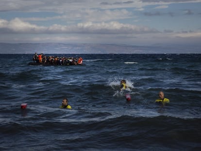 Llegada de botes atestados de refugiados a la isla de Lesbos y, en primer plano, tres socorristas para ayudarlos.
