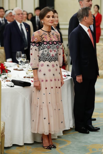 Para una cena de gala durante el viaje de los reyes a Corea del Sur, doña Letizia añadió una nueva marca a su vestidor: Temperley London, la firma favorita de Kate Middleton, duquesa de Cambridge. Se trata de un vestido 'midi', de escote transparente y con bordados florales geométricos. Lo combinó con unos salones de Manolo Blahnik y una cartera de mano de raso negro de Magrit.